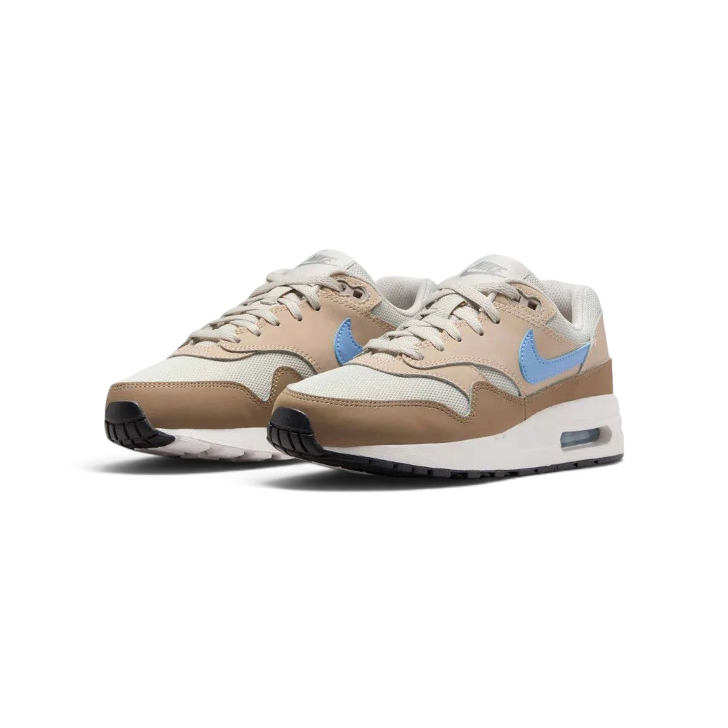 Angled view of two Nike Air Max 1 Juniors' trainers in light bone, psychic blue, and black, side by side, showcasing their timeless design and layered upper.