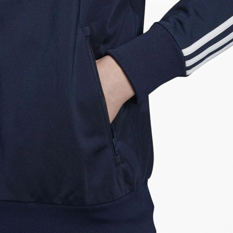 Close-up zoom on the Adidas Firebird Track Jacket Men's, showing the smooth tricot fabric texture and the 3 stripes on the arm with hand in pocket