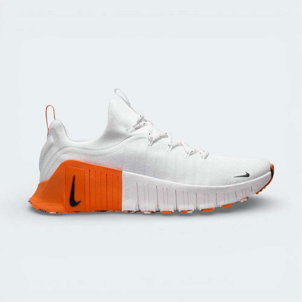 Side profile of the Nike Free Metcon in white, showing the black Swoosh, Safety Orange accents, and the transition between the flexible forefoot and stable heel.