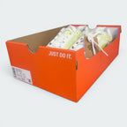 The Nike Air Winflo 11 shoes sitting inside an open orange Nike shoebox with no lid, displaying the classic slogan "JUST DO IT." in white on the side of the box and a circular-logo brown paper tag tied to the laces.