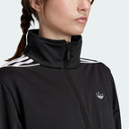 Close-up zoom on the Adidas Women's Archival Track Jacket in black, showing the smooth knit fabric texture and the embroidered white Trefoil logo detail on the chest.