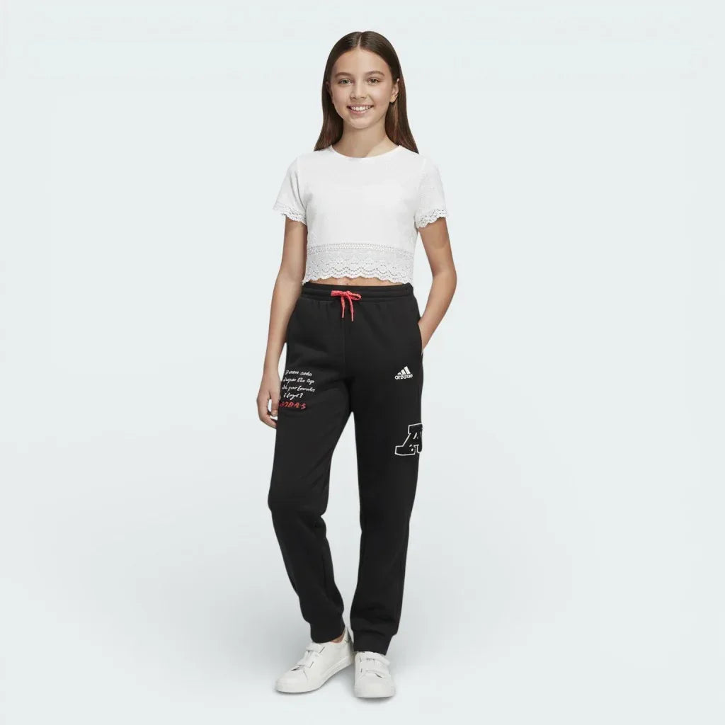 Person wearing a white crop top and black Adidas pants on a white background Main image