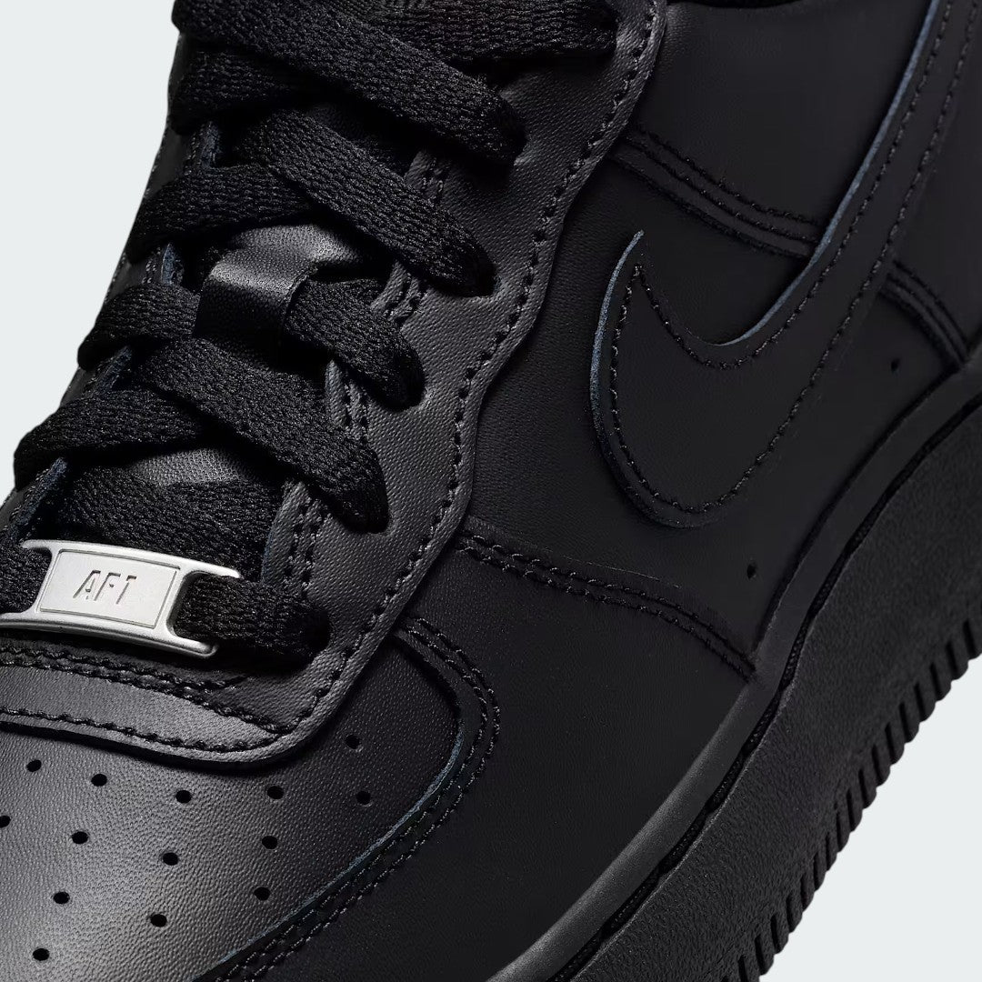 Close-up zoom on the front of the Nike Air Force 1 Juniors' black trainers, showing the perforated toe box, lacing system, and texture of the leather upper.
