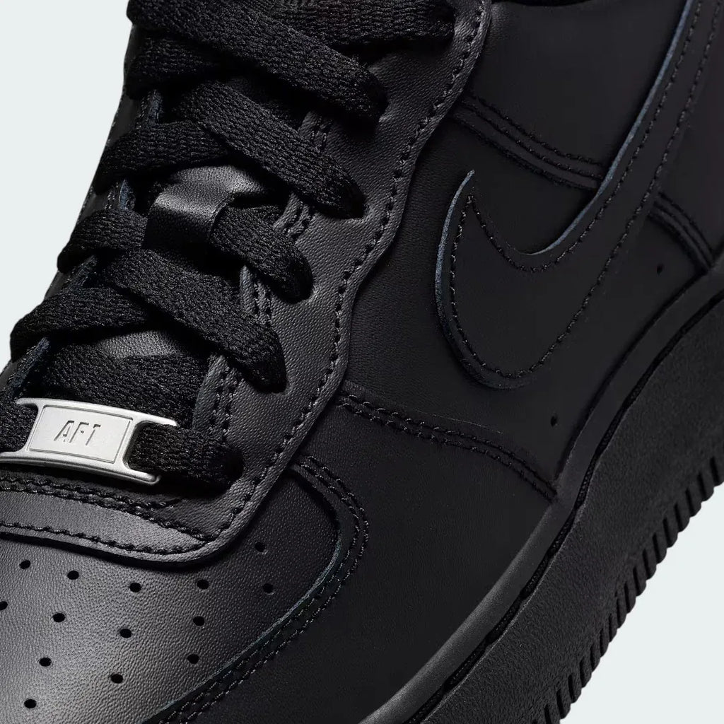 Close-up zoom on the front of the Nike Air Force 1 Juniors' black trainers, showing the perforated toe box, lacing system, and texture of the leather upper.