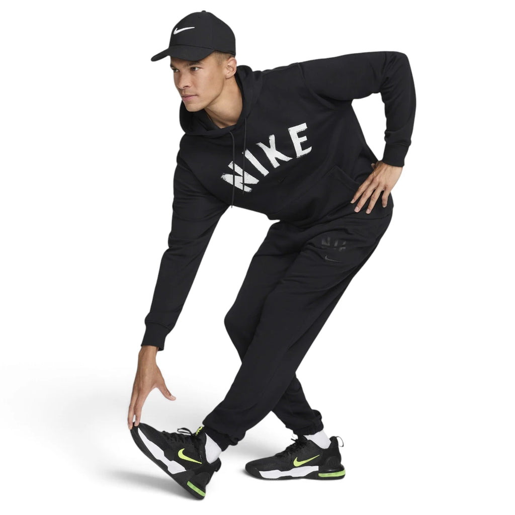 Dynamic action shot of a male model wearing the complete black Nike training outfit, demonstrating the flexibility and range of movement provided by the midweight Dri-FIT French terry fabric during a stretch pose.