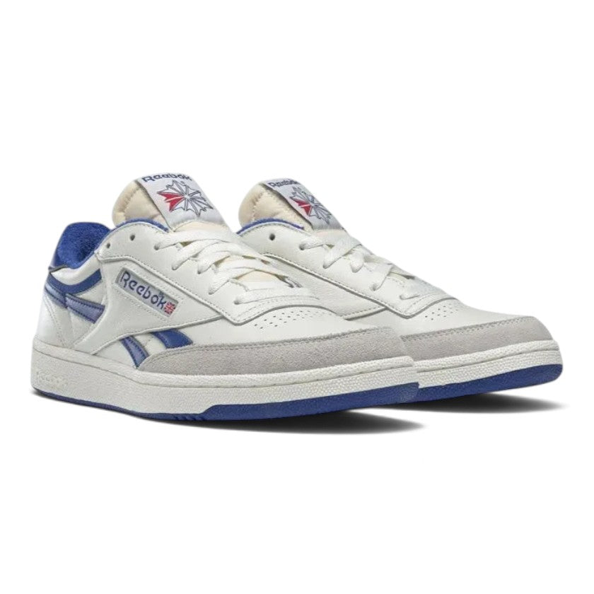 Three-quarter angled view of both Reebok Club C Revenge Vintage shoes positioned side by side, showcasing the chalk leather uppers, grey suede mudguards, royal blue detailing, and vintage woven tongue labels.