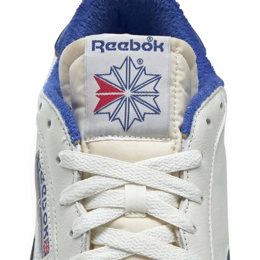 Close-up detailed shot of the front shoe tongue and laces, showing the vintage Reebok woven label with classic Union Jack and Starcrest logo, cream exposed foam tongue edge, and white flat laces.