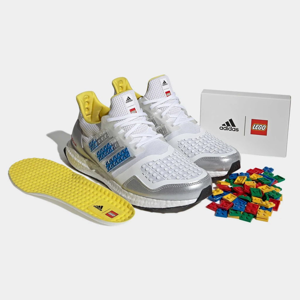 Angled view of two Adidas Ultraboost DNA x Lego Men's trainers in white and blue, side by side, showcasing their bold design and Lego-inspired details.