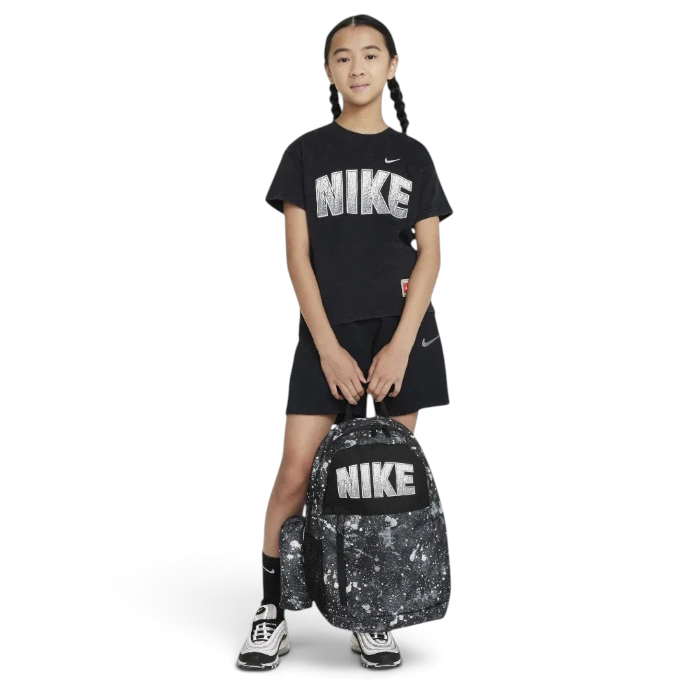 Person wearing a black Nike t-shirt and shorts, holding a black and white Nike backpack on a light gray background
