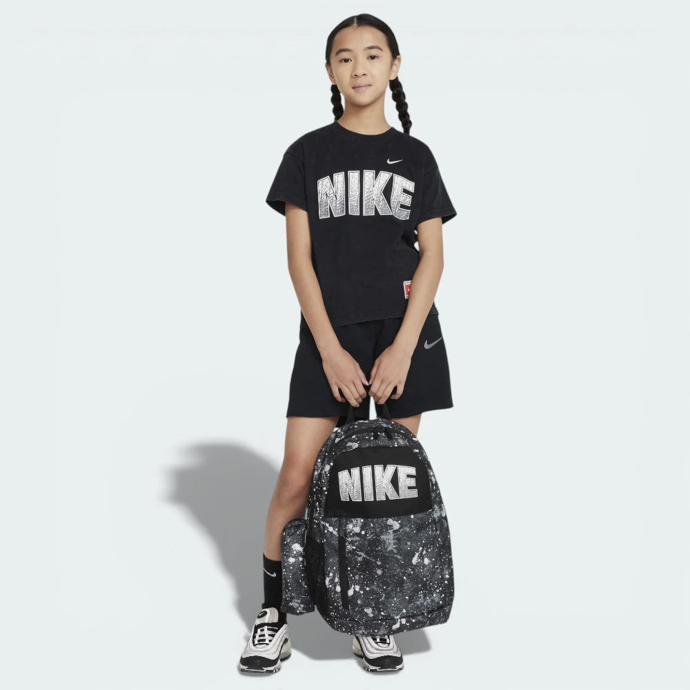 Person wearing a black Nike t-shirt and shorts, holding a black and white Nike backpack on a light gray background