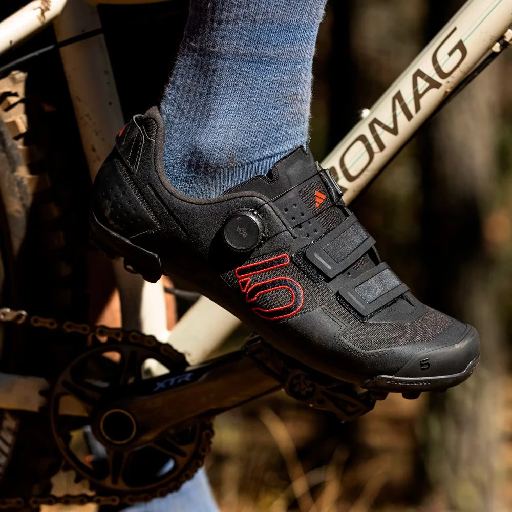 Black cycling shoe with red logo on a mountain bike, blurred natural background
