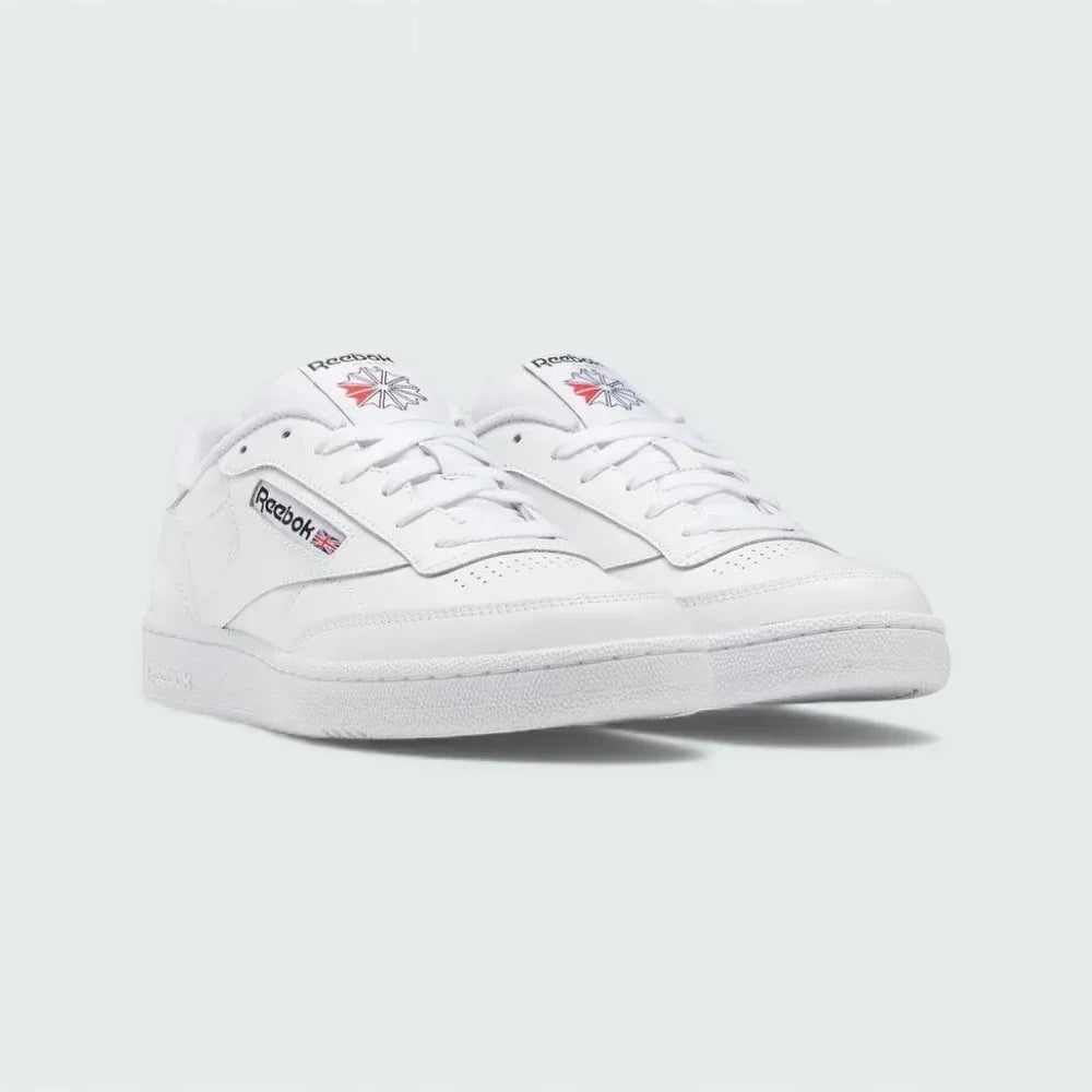 Angled view of two Reebok Classic Club C 85 Unisex white trainers, side by side, showcasing their timeless aesthetic and classic court design.
