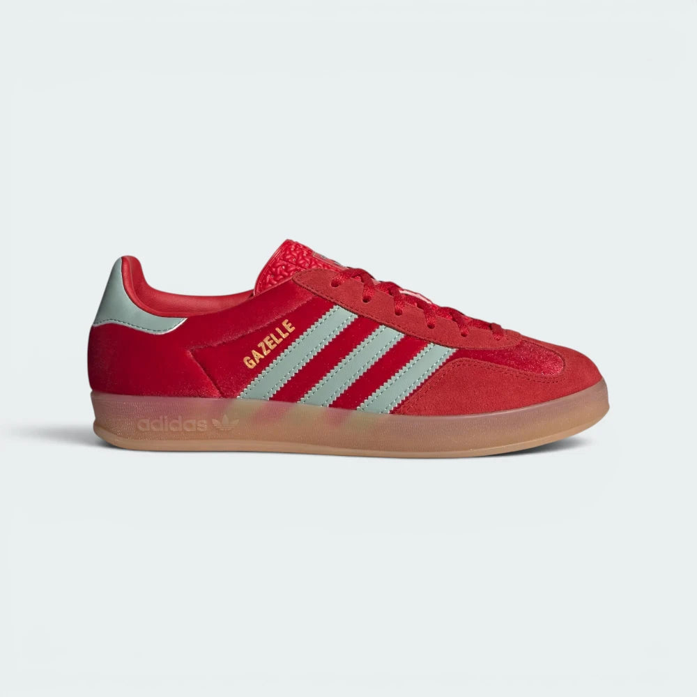 Highlights the high-velocity sweep of the Hazy Green serrated 3-Stripes, the gleaming gold-foil Gazelle text, and the professional, plush depth of the Better Scarlet velvet panels leading down to the translucent gum rubber sole.