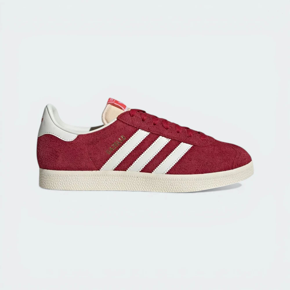 The Team Victory Red Gazelle, highlighting the Off White 3-Stripes and the gleaming Gold Metallic wordmark. Main image