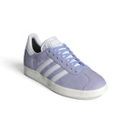 Forward three-quarter angle showcasing the trainer propped up, highlighting the low-slung terrace stance, velvety matte suede texture, flat violet laces, and timeless purple-and-white contrast.