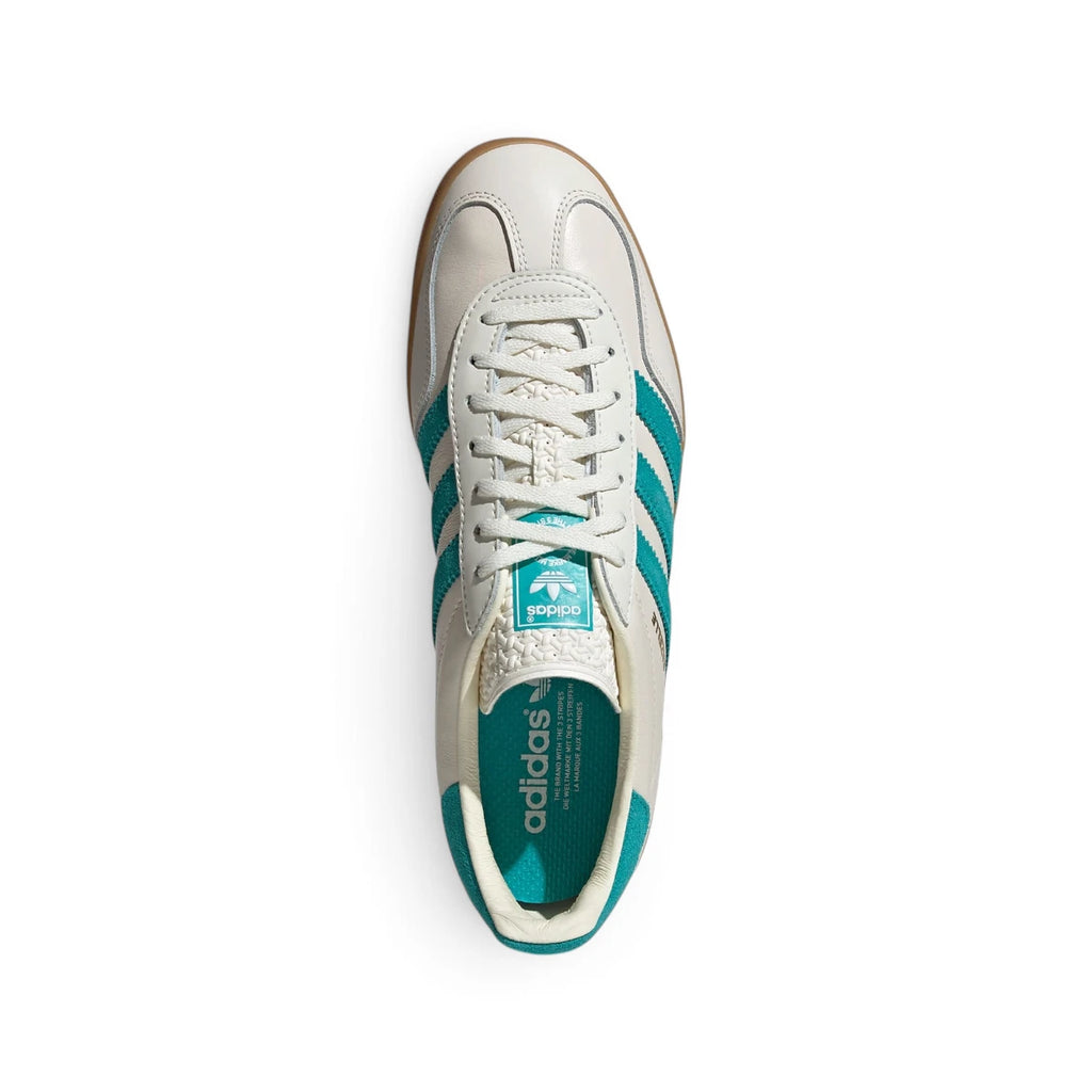 Overhead view looking down at the laced white shoes, displaying the flat white laces, textured tongue label with the teal Trefoil logo, and branded insole.