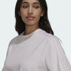 Close-up zoom on the fabric of the Adidas Tennis Luxe Tee Dress in ambient blush pink, showing the soft cotton jersey texture and any embroidered Adidas logo detail.