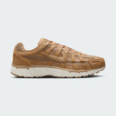 Nike P-6000 SE men's trainers in flax (light brown) with metallic gold accents, side profile showing layered mesh and leather/suede overlays.