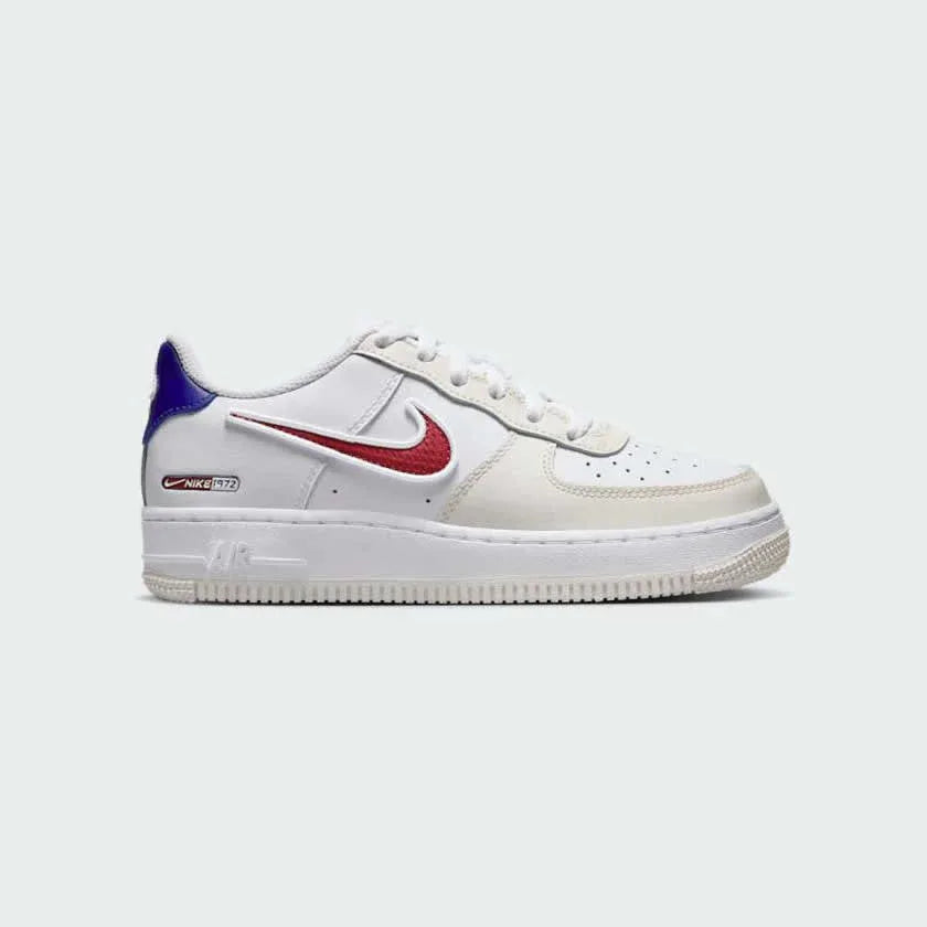 Nike Air Force 1 LV8 Juniors' trainers in white with royal blue and red accents, side profile showing classic leather upper, perforated toe box, and Nike Swoosh. Main image
