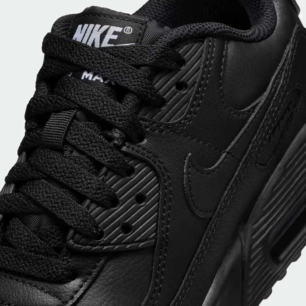 Close-up zoom on the front of the Nike Air Max 90 Juniors' black trainers, showing the mesh toe box, lacing system, and layered synthetic overlays.