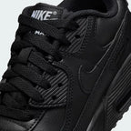Close-up zoom on the front of the Nike Air Max 90 Juniors' black trainers, showing the mesh toe box, lacing system, and layered synthetic overlays.
