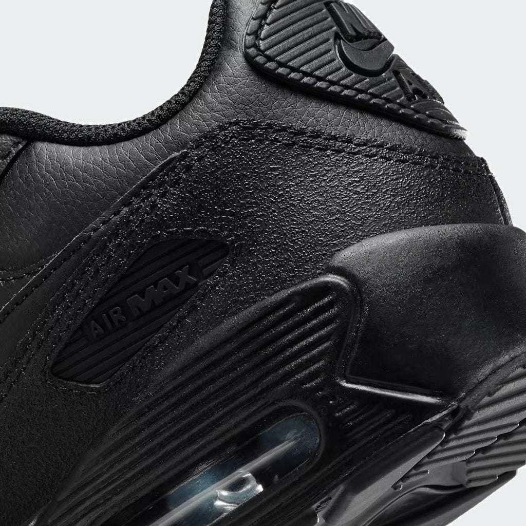 Detailed zoom on the outsole and midsole of the Nike Air Max 90 Juniors' black trainers, highlighting the cushioned foam and visible Max Air unit.