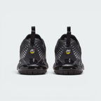 Focuses on the rear profile, highlighting the dual black pull tabs, circular yellow-and-black "AIR MAX" badges, and the translucent black heel clip framing the yellow Air bubble.