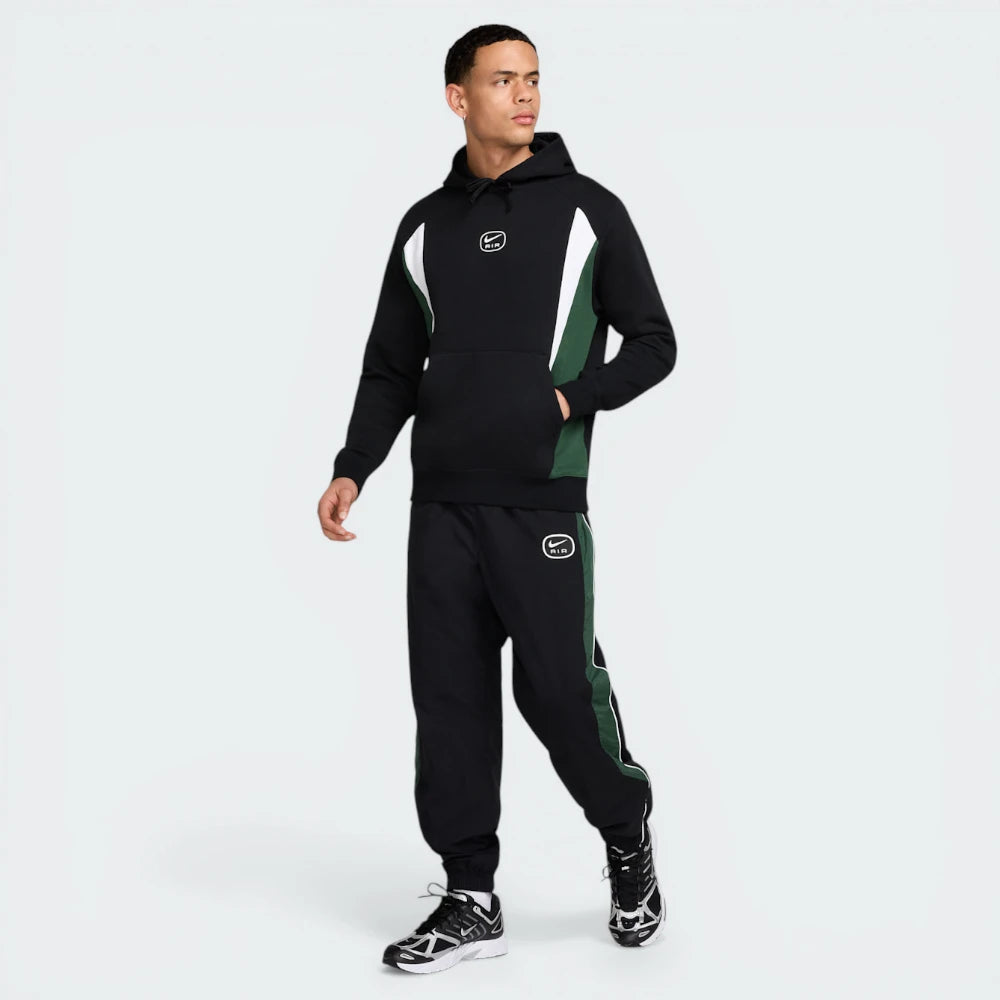 Man wearing a black and green tracksuit with brand logos on a white background