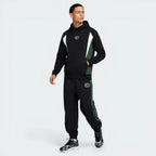 Man wearing a black and green tracksuit with brand logos on a white background