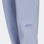 Close-up zoom on the Adidas Trefoil Linear Sweat Pants in violet, showing the soft fleece fabric texture and the detailed linear Trefoil logo print on the leg.