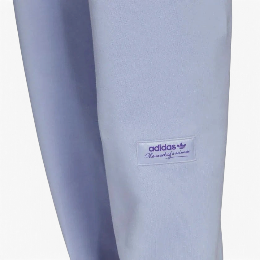 Close-up zoom on the Adidas Trefoil Linear Sweat Pants in violet, showing the soft fleece fabric texture and the detailed linear Trefoil logo print on the leg.