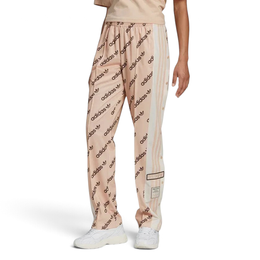 Trade Sports Adidas women's Adibreak track pants in halo blush with allover monogram logos and side snap buttons.