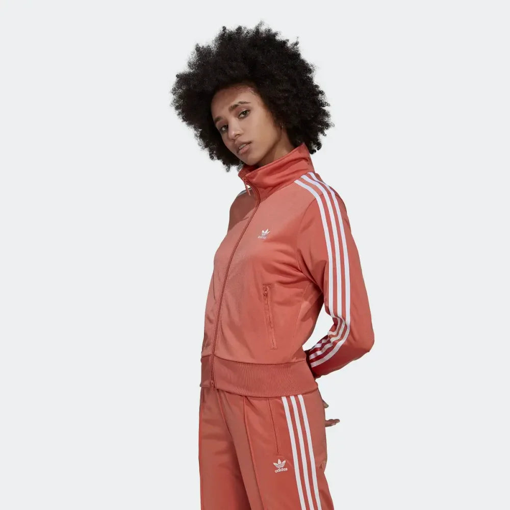 Side profile of the Adidas Firebird track top in Magic Earth brown, showing the classic white 3-Stripes running from the shoulder to the ribbed cuff.