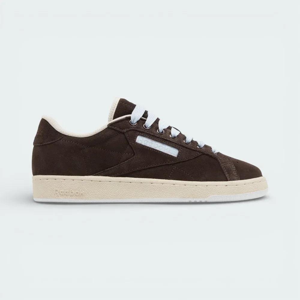 Side profile of the Reebok x SNEEZE Club C Grounds in Earth brown suede, showing the tonal side stripes and the contrasting Stucco white rubber outsole. Main image