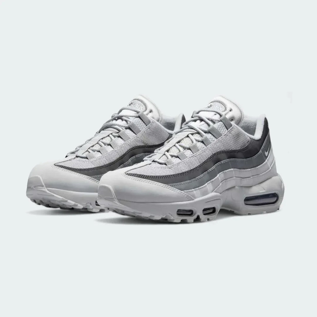 Angled view of two Nike Air Max 95 Men's running shoes in shades of grey, side by side, showcasing their timeless design and layered upper.