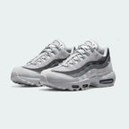 Angled view of two Nike Air Max 95 Men's running shoes in shades of grey, side by side, showcasing their timeless design and layered upper.