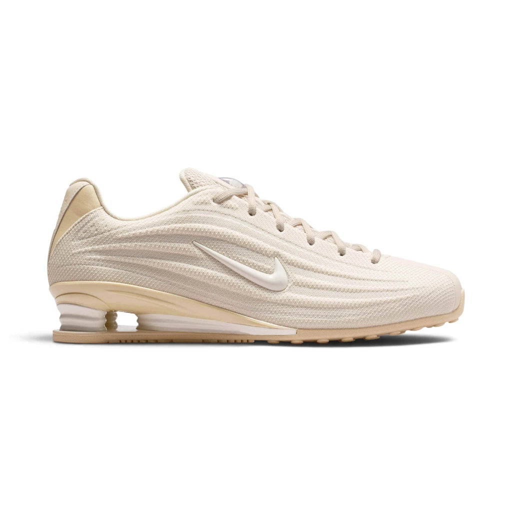 Side Profile Image: Studio lateral shot of the Nike Women's Shox Z in Oatmeal and Phantom Linen, highlighting the textured neutral mesh upper, sculpted synthetic mudguard, miniature white Swoosh, and iconic Shox cushioning columns in the heel.   