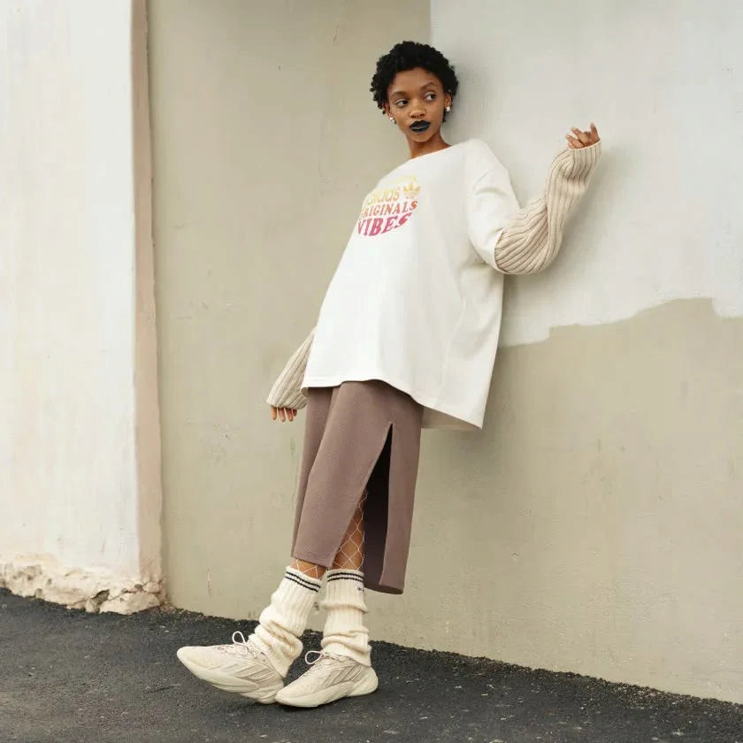 Trade Sports model wearing an Adidas chalk white boyfriend t-shirt with ribbed sleeves, brown skirt, and leg warmers.