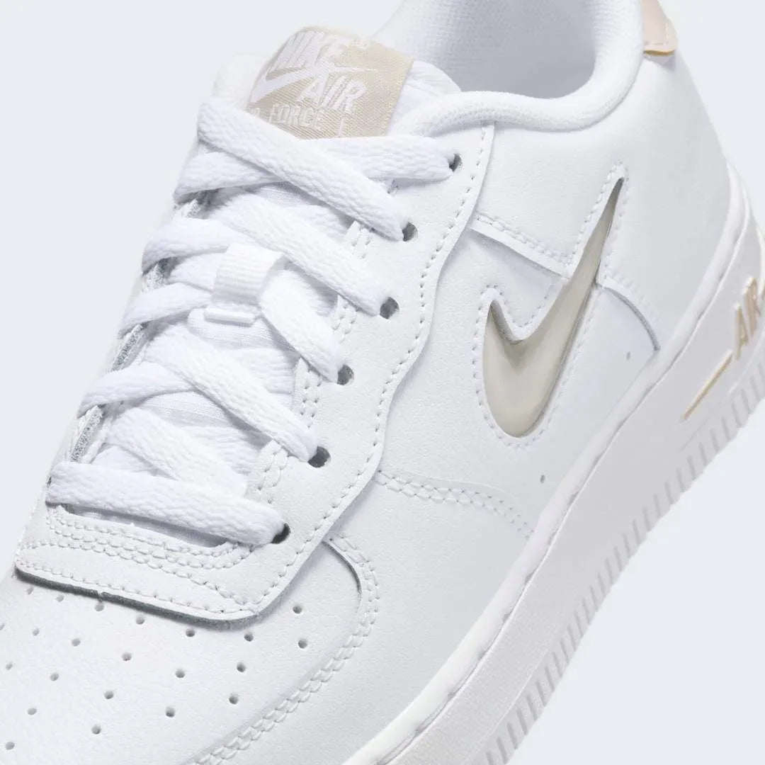 Close-up zoom on the front of the Nike Air Force 1 Low Juniors' white/sand trainers, showing the perforated toe box, lacing system, and texture of the leather upper.
