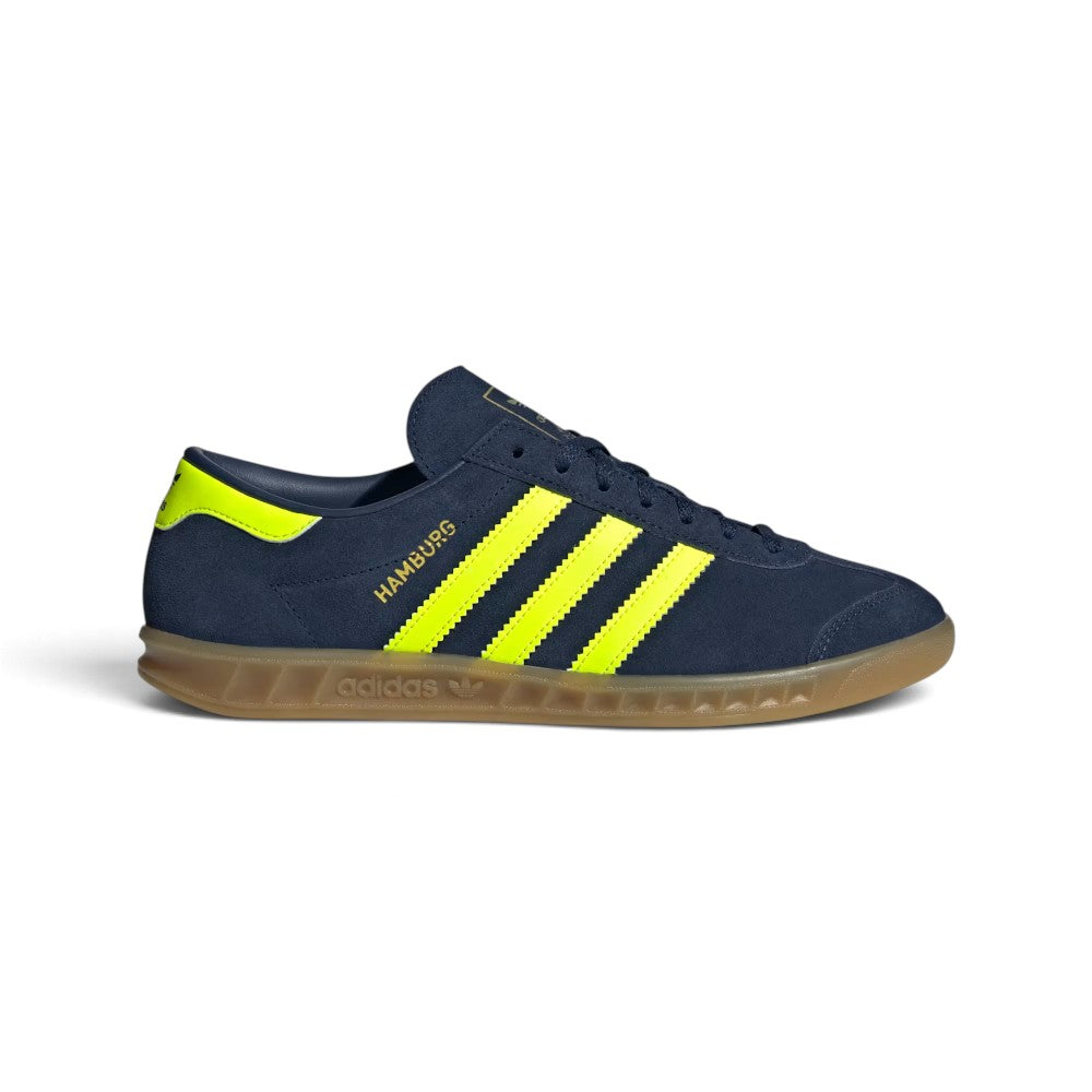 Highlights the sleek low-profile lateral silhouette featuring the rich Night Indigo suede upper, vibrant Solar Yellow leather serrated 3-Stripes, metallic gold foil "HAMBURG" script, matching yellow heel tab, and semi-translucent gum rubber cupsole with debossed adidas Trefoil branding.