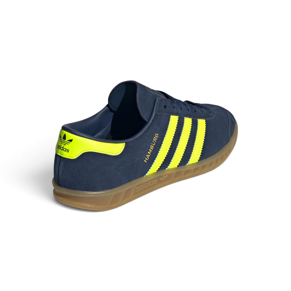 Focuses on the rear three-quarter profile, displaying the vibrant Solar Yellow leather heel moustache tab stamped with an indigo Trefoil logo, clean heel counter stitch lines, and the textured rim of the translucent gum cupsole.