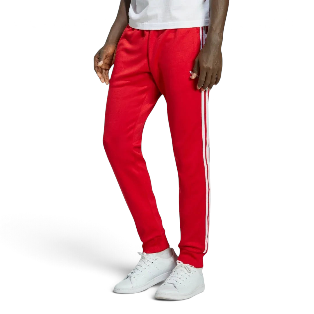 Adidas Superstar Track Pants Men's in red, front view showing white 3-Stripes down the legs, Trefoil logo on the hip, and zipped pockets. Main image