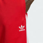 Close-up zoom on the Adidas Superstar Track Pants Men's in red, showing the smooth tricot fabric texture and the embroidered white Trefoil logo detail.