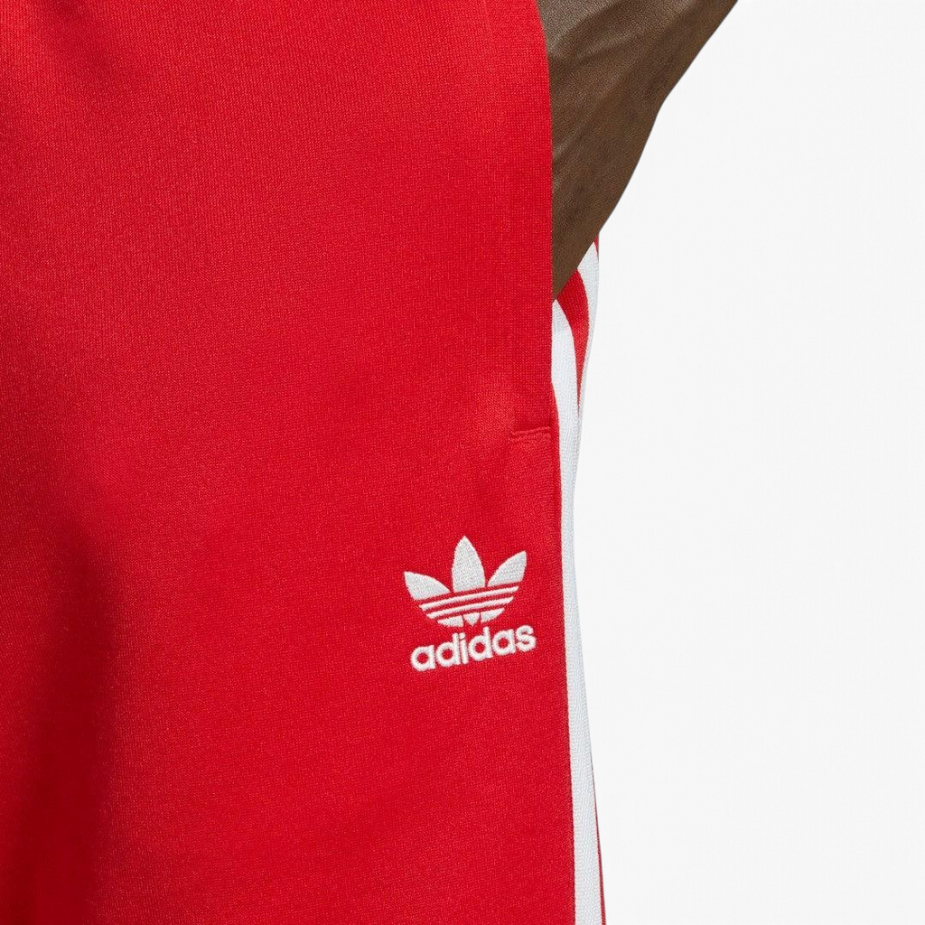 Close-up zoom on the Adidas Superstar Track Pants Men's in red, showing the smooth tricot fabric texture and the embroidered white Trefoil logo detail.