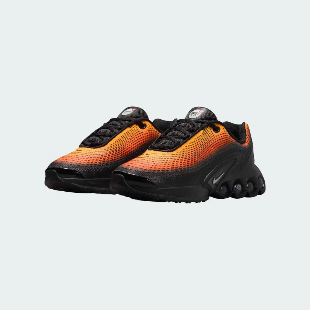 Angled view of two Nike Air Max DN Juniors' black running trainers, side by side, showcasing their bold, modern design and prominent Air unit.