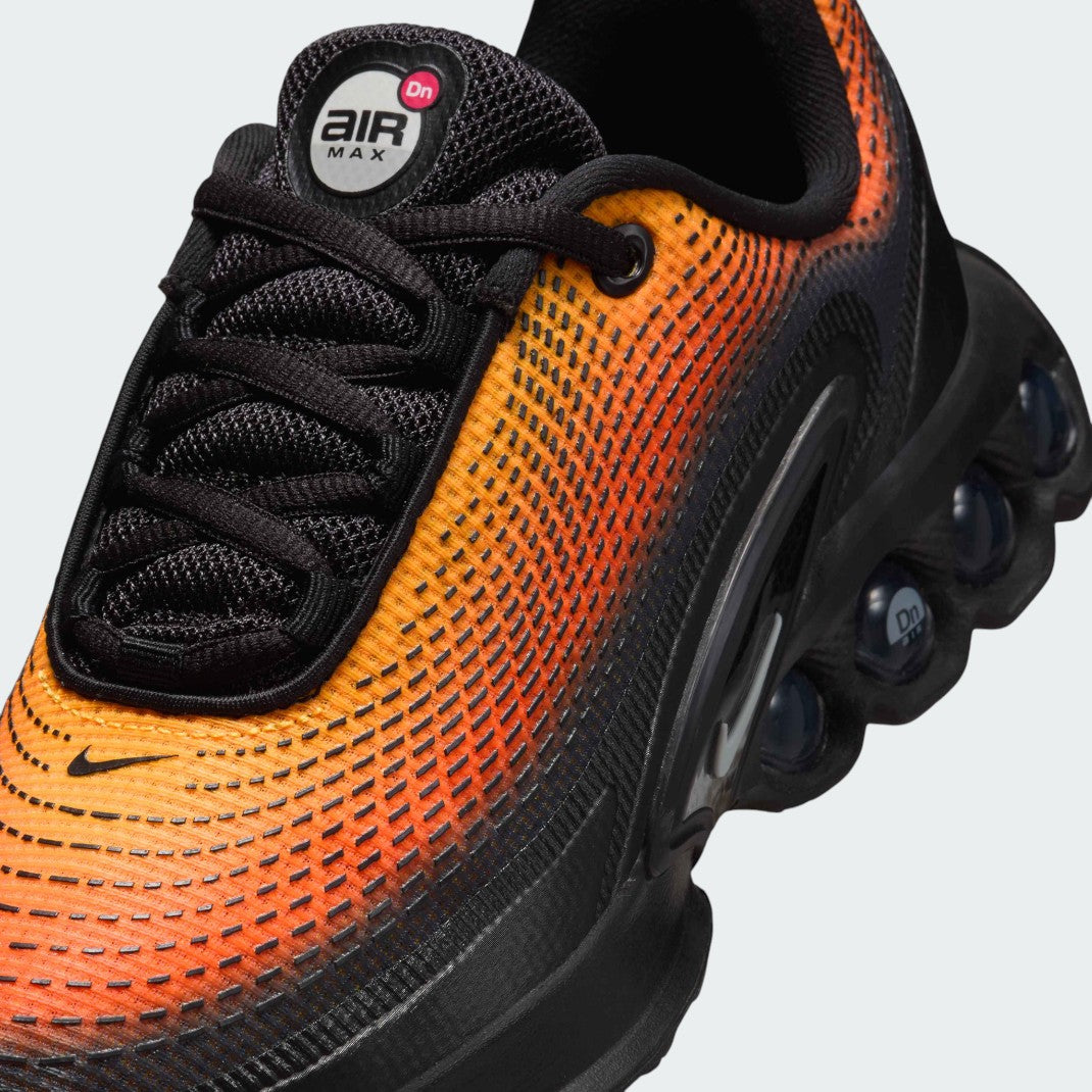 Close-up zoom on the front of the Nike Air Max DN Juniors' black running trainers, showing the mesh upper texture, haptic print details, and lacing system.