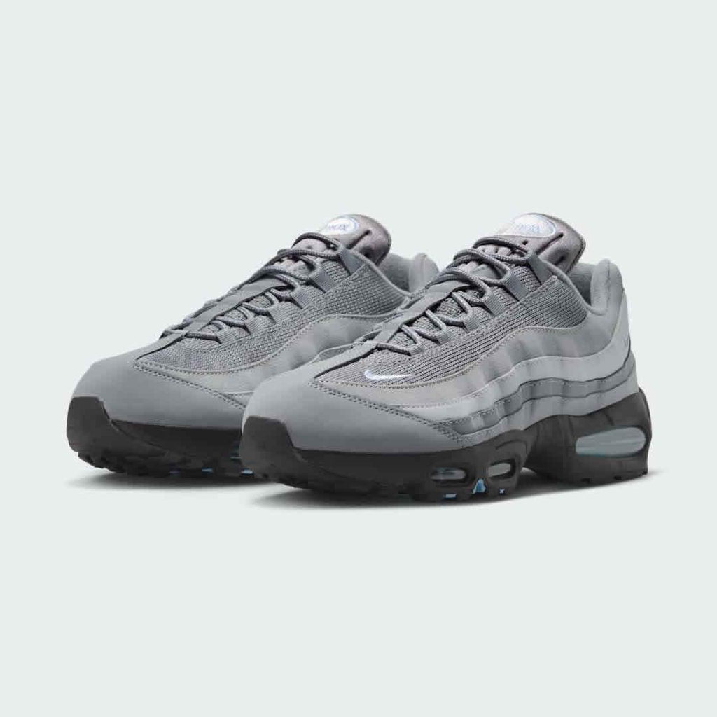 Angled view of two Nike Air Max 95 OG Men's running shoes in grey, red, and black, side by side, showcasing their timeless design and layered upper.