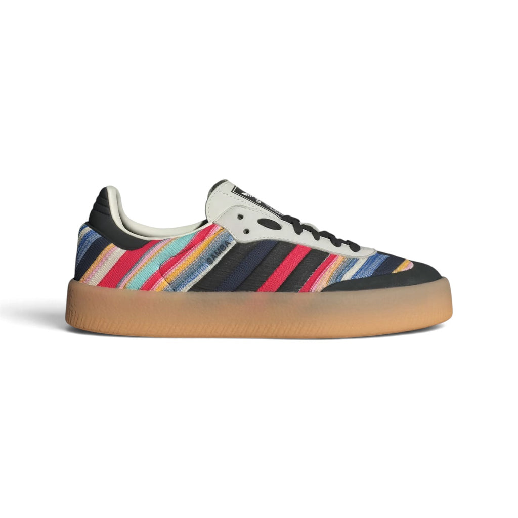 Side Profile Image: Studio lateral shot of the KSENIASCHNAIDER x adidas Originals Sambae in ivory, core black, and multicolored stripes, highlighting the reworked textile upper, embroidered three stripes, black toe cap, and signature gum rubber platform outsole.   