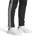 On-Foot Lifestyle View: Full-length shot of the sneakers worn with black track trousers, highlighting their low-profile tennis silhouette and modern proportions.