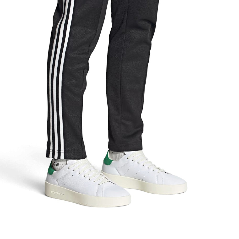 On-Foot Lifestyle View: Full-length shot of the sneakers worn with black track trousers, highlighting their low-profile tennis silhouette and modern proportions.